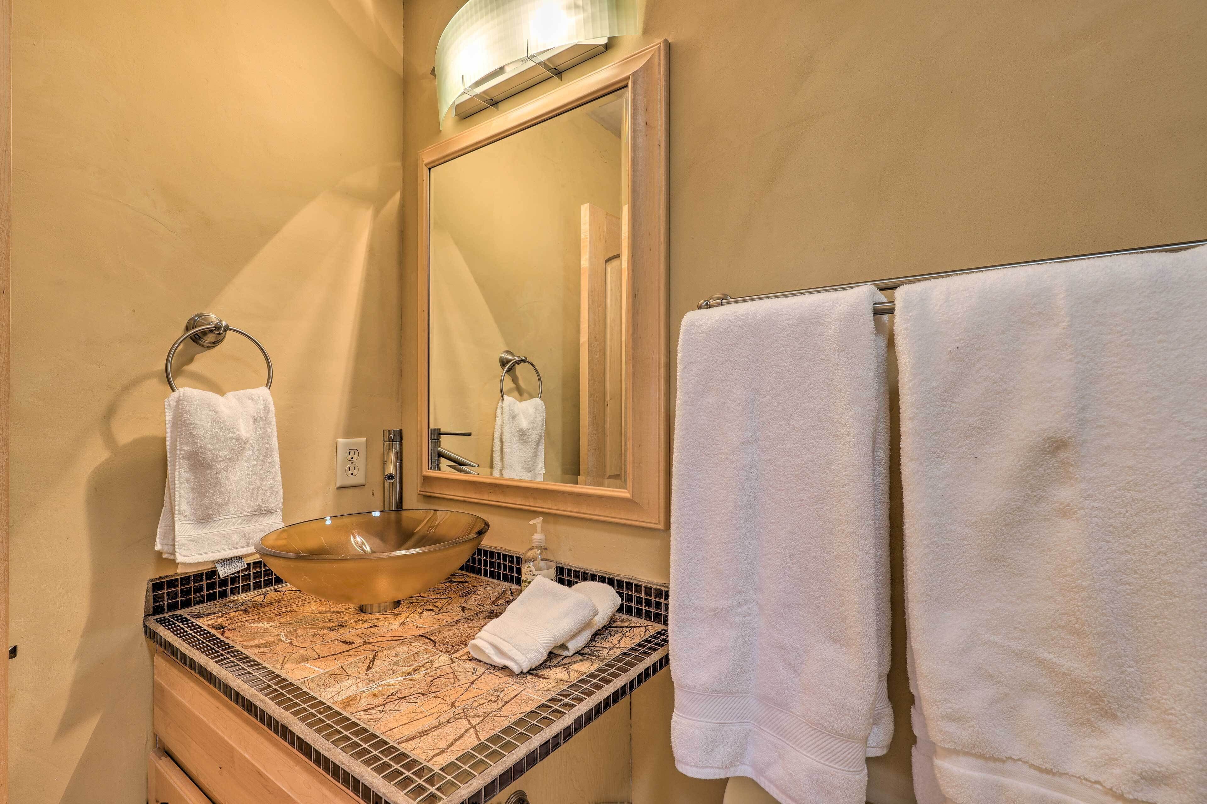 A bathroom with a large mirror, a vessel sink, and two towels hanging on the wall.