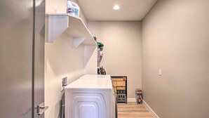 Une buanderie équipée d’un lave-linge et d’un sèche-linge à chargement frontal, d’une étagère contenant des produits de nettoyage et d’un petit espace de rangement avec des boîtes.
