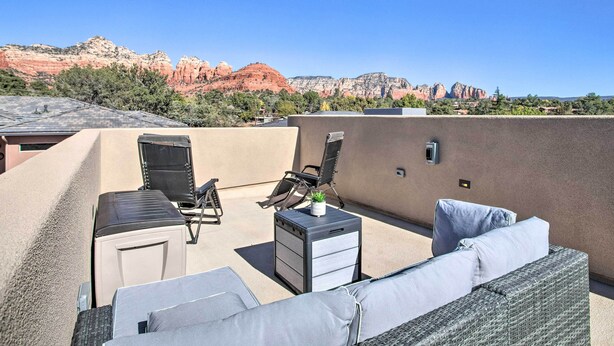 Une terrasse sur le toit, aménagée avec un canapé, des chaises, une petite table et un buffet. La terrasse offre une vue panoramique sur des formations rocheuses rouges spectaculaires.