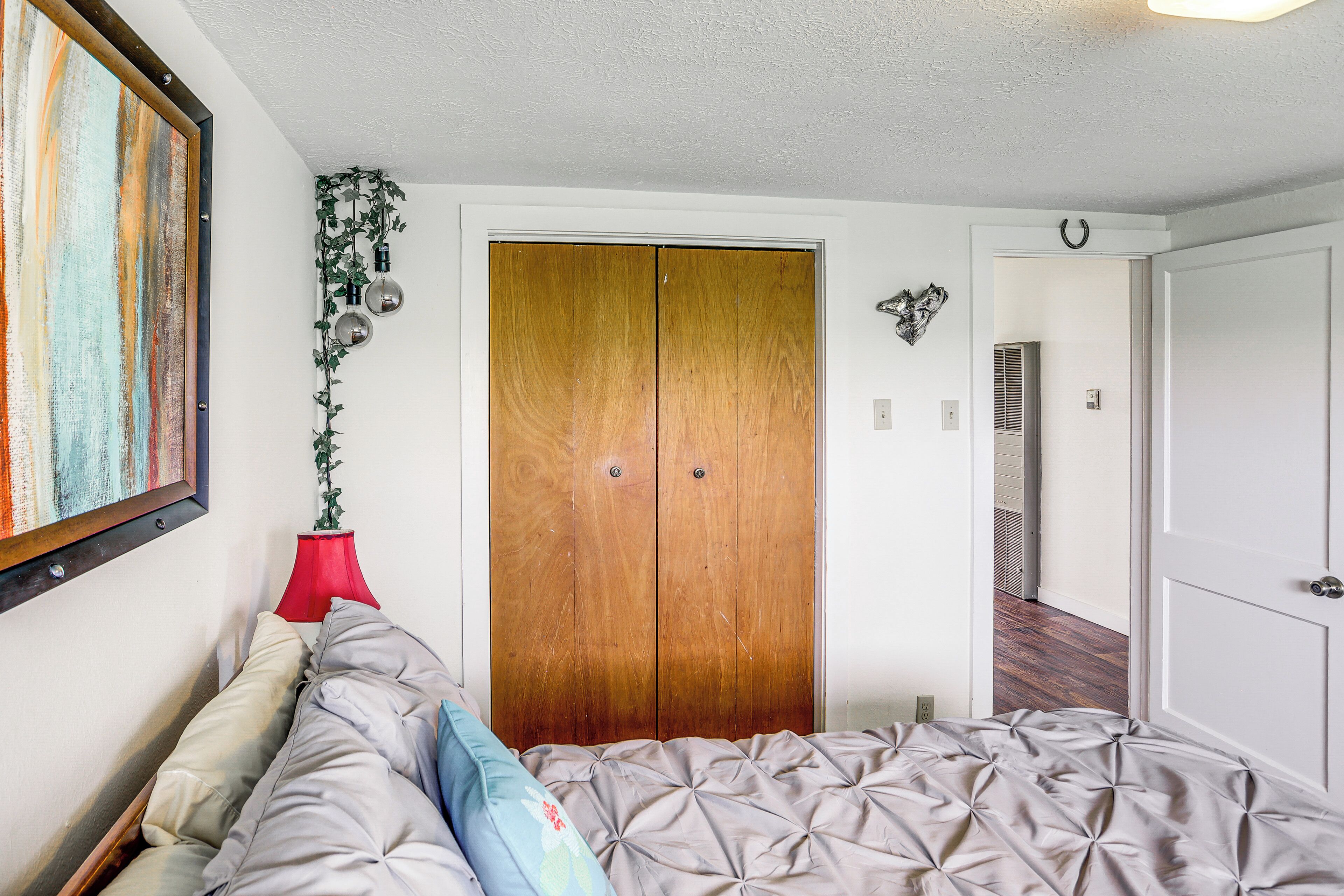 Un dormitorio con una cama, un armario de madera, una lámpara roja y un cuadro en la pared.