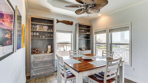 Un coin repas avec une table en bois et des chaises blanches, un élément décoratif en forme de poisson sur le mur et un ventilateur de plafond.