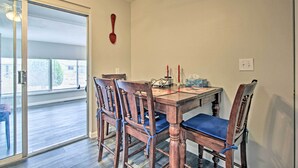 Un coin repas avec une table et des chaises en bois, une porte-fenêtre coulissante donnant sur un balcon et un luminaire fixé au mur.