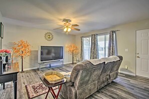 A living room with a grey sofa, a flat-screen TV, a ceiling fan, and two artificial trees. - 6 Mi to State Farm Stadium: Wfh-friendly Home! (Sun City)