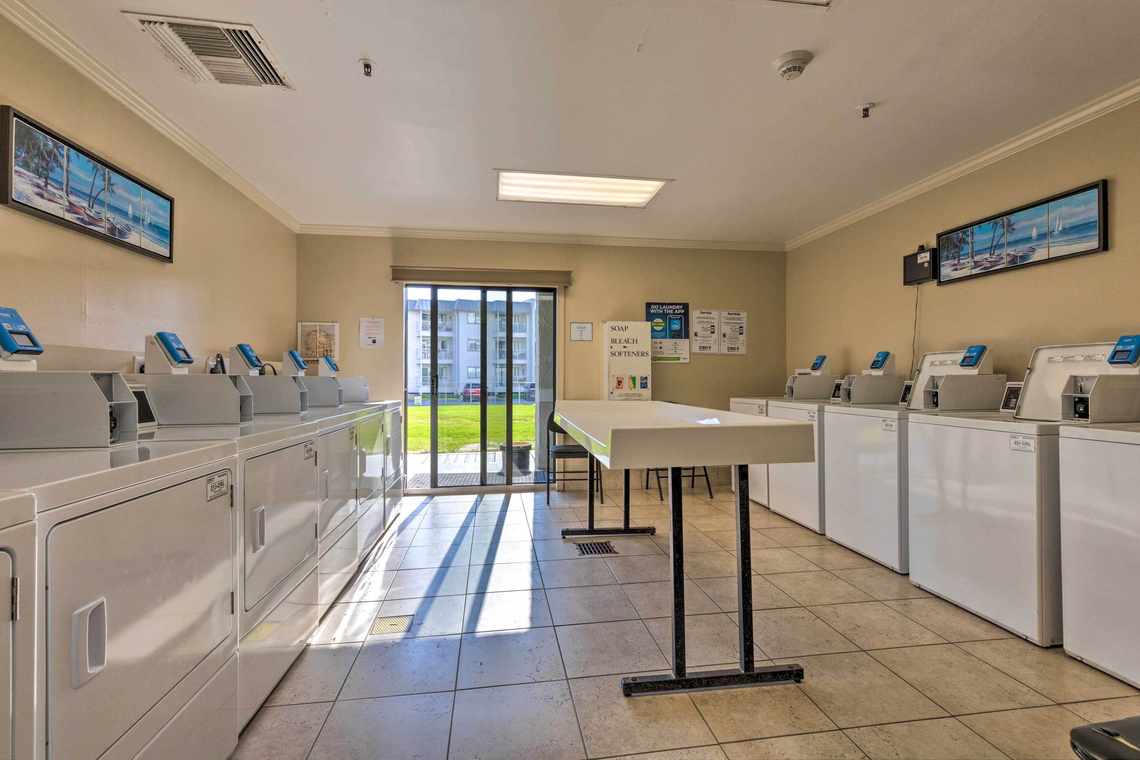 A laundry facility with multiple washing machines and dryers, a table, and a view of the outside.