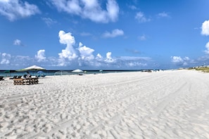 A wide sandy beach with footprints, a few umbrellas, and a clear blue sky. - Relaxing Gulf Shores Condo w/ Beach-view Balcony (Gulf Shores)