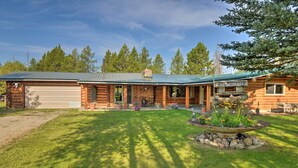Eine Blockhütte mit einer Veranda, einer Garage und einem begrünten Vorgarten mit Blumenbeeten.