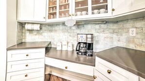 Een keuken met witte kastjes, een koffiezetapparaat en een betegelde spatwand.