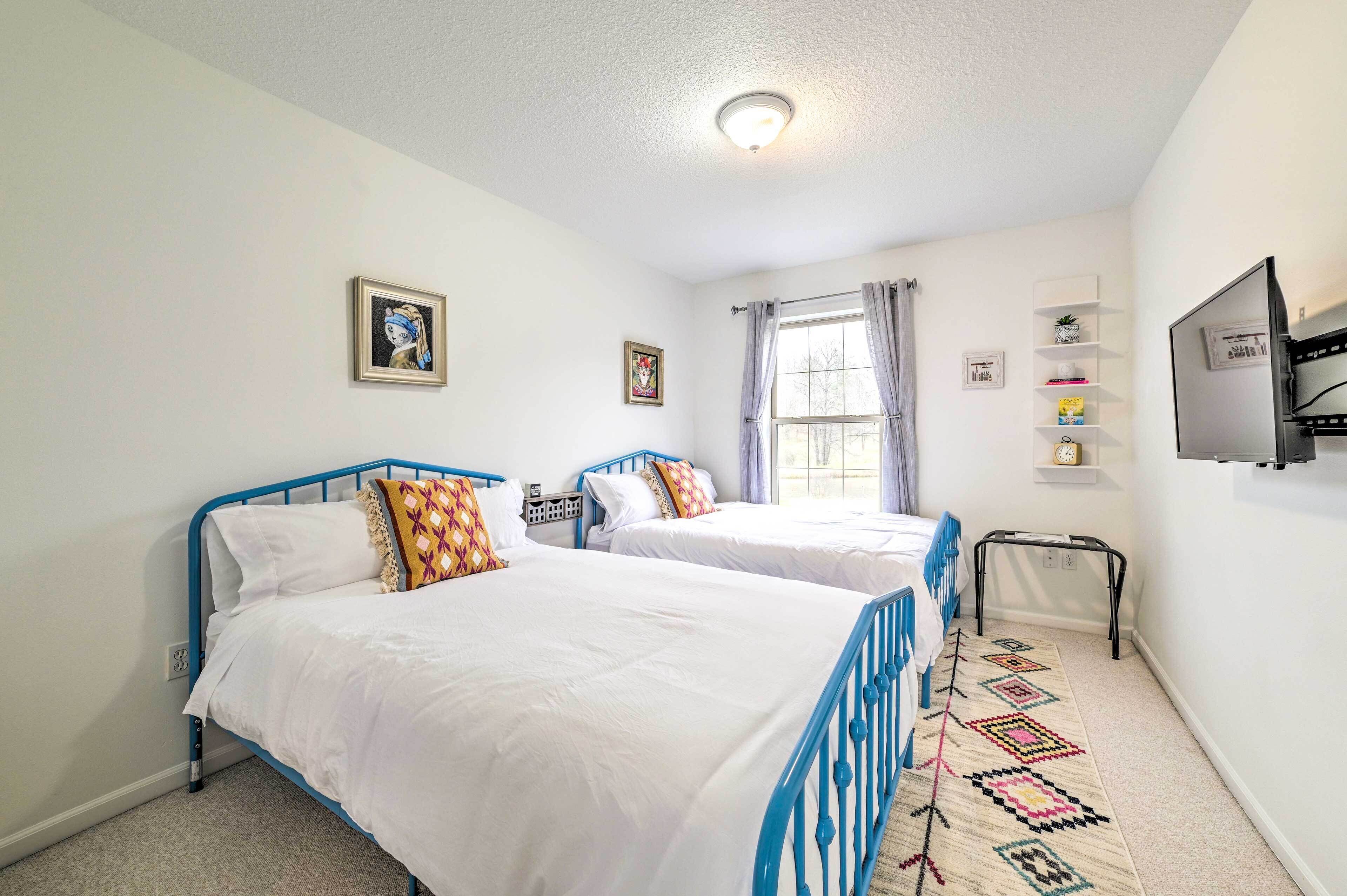 A bedroom with two beds, a TV, a window with curtains, and a shelf with books and decorative items.