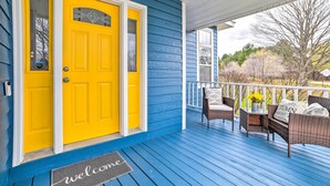 Een blauw huis met een gele deur, een veranda met rieten meubels en een welkomstmat.