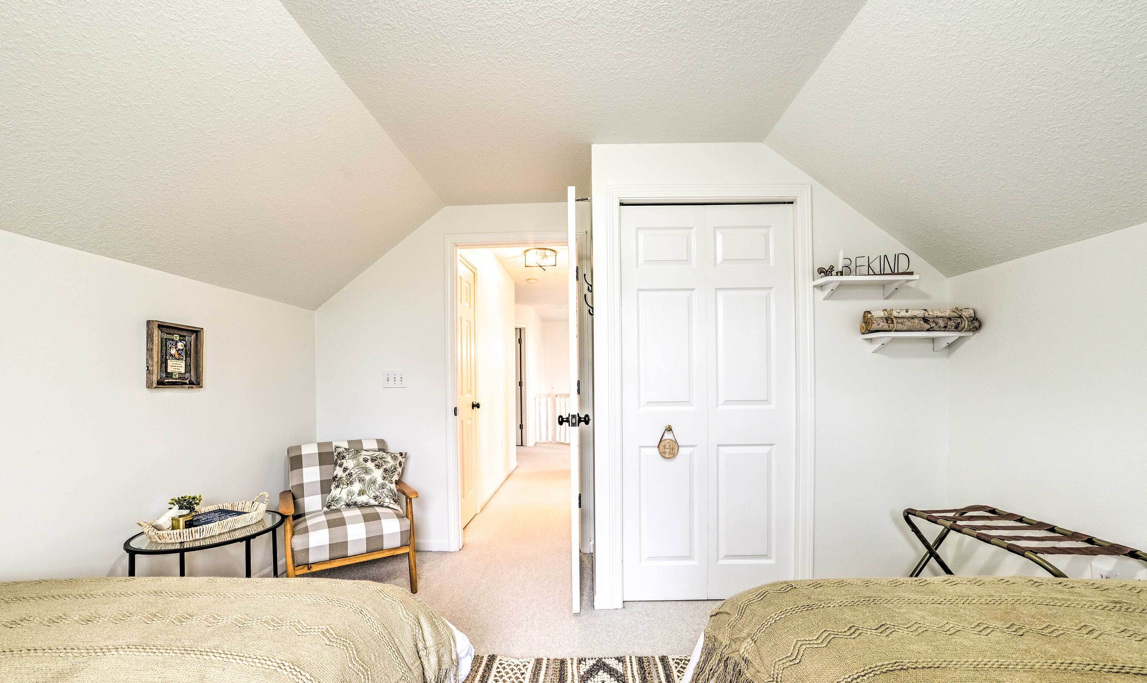 A cozy bedroom with a checkered armchair, a small table with a basket, a white door, and a shelf with decorative items.