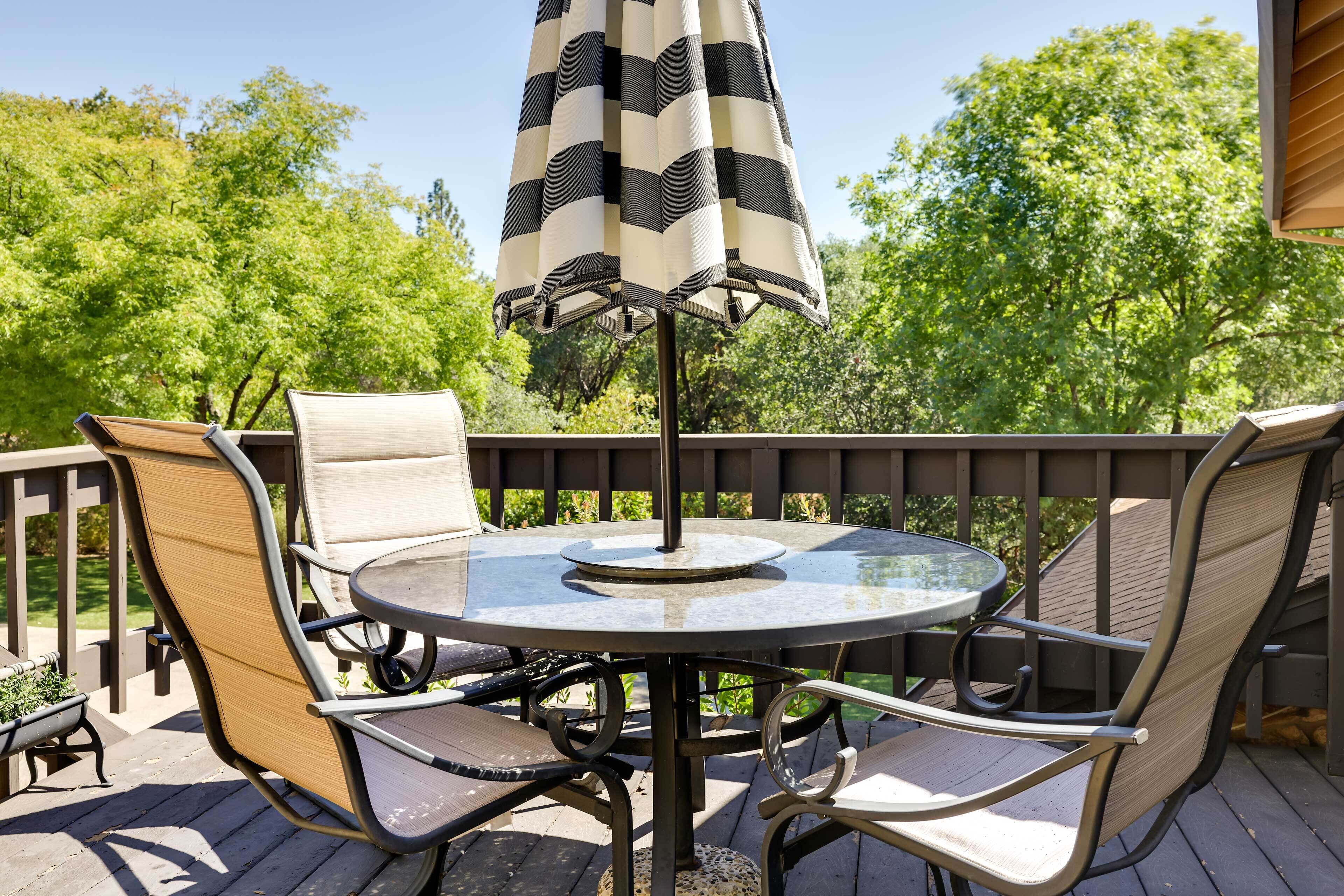 A round glass table with four chairs and a striped umbrella on a wooden deck.