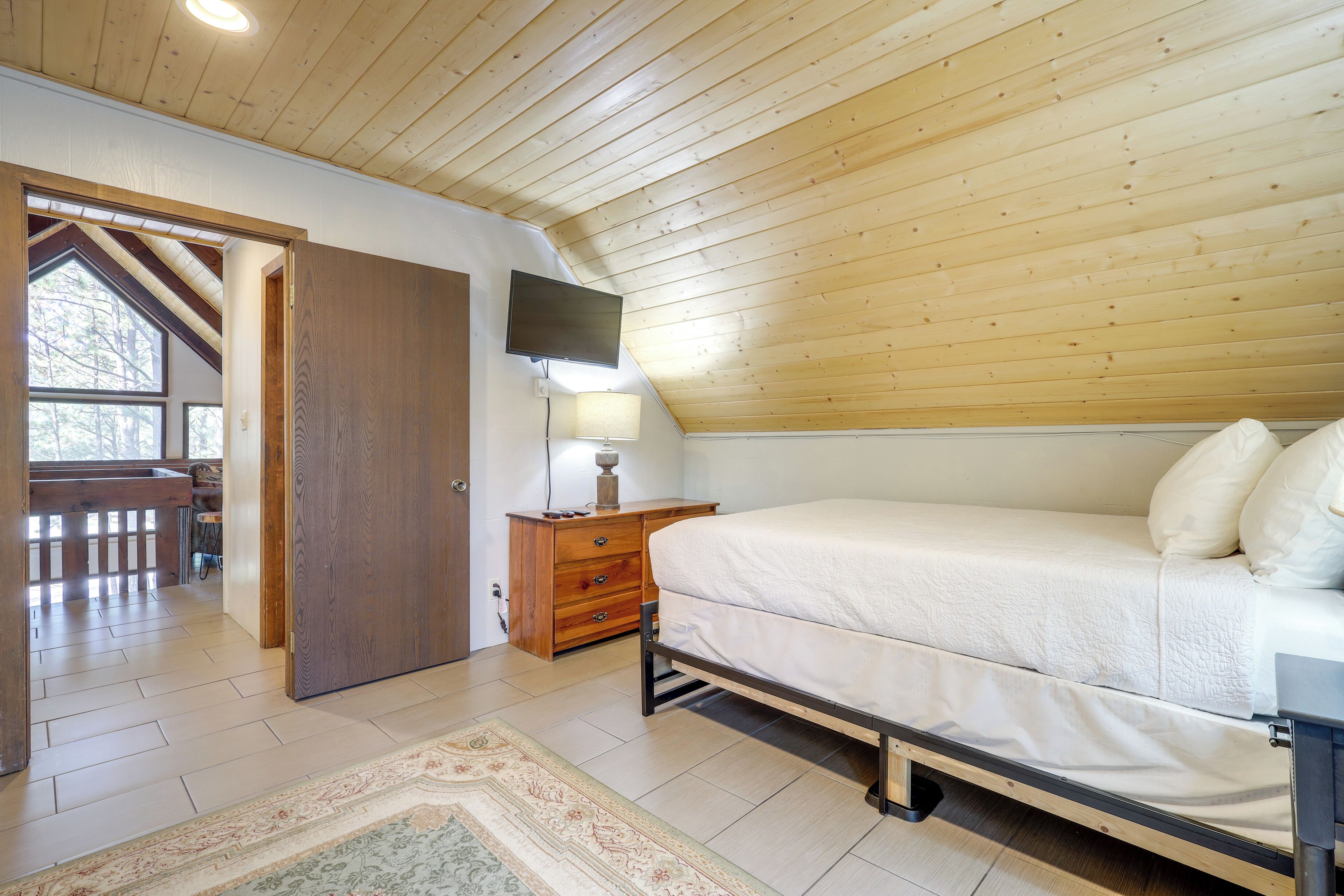 Ein Schlafzimmer mit Holzboden, einem Bett, einem Nachttisch, einem Fernseher und einem Fenster.