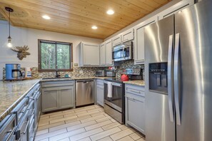 A modern kitchen with stainless steel appliances, a wooden ceiling, and a large window. - Deluxe A-frame Home w/ Game Room & Deck! (Angel Fire)