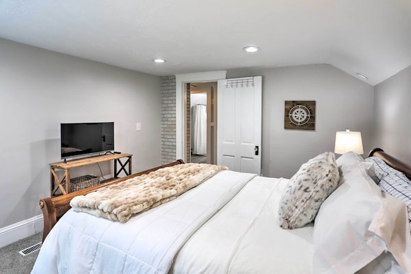 A bedroom with a bed, a television on a wooden stand, a white door, and a wall-mounted light. - Pet-friendly Home - 1/2 Mi to Downtown Willoughby! (Willoughby)