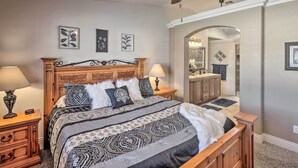 A bedroom with a wooden bed, two bedside tables with lamps, a ceiling fan, and framed artwork on the walls. - Lake Havasu City House w/ Fire Pit, Pool & Spa! (Lake Havasu City)
