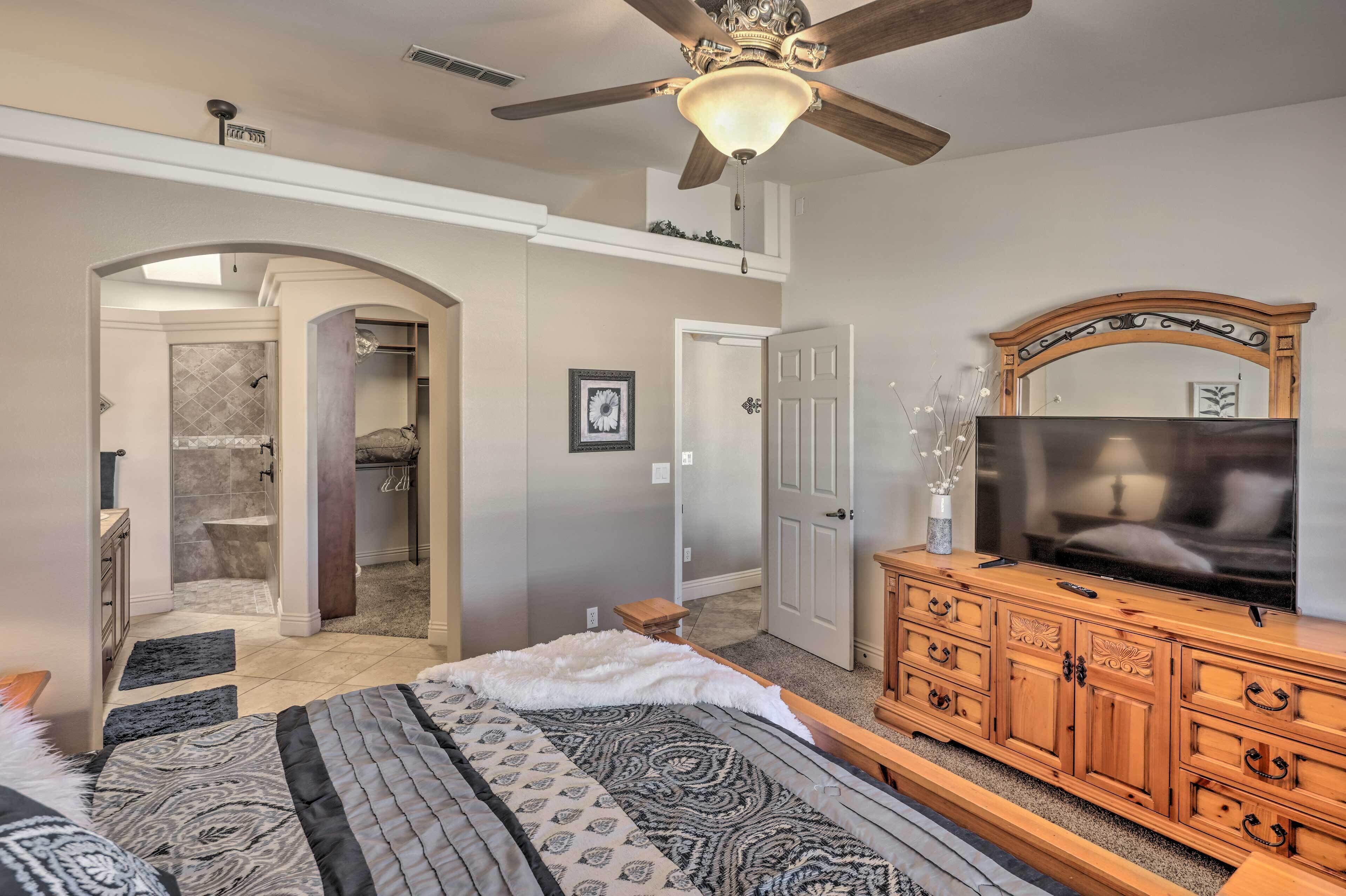 A bedroom with a bed, a wooden dresser, a television, and a ceiling fan.