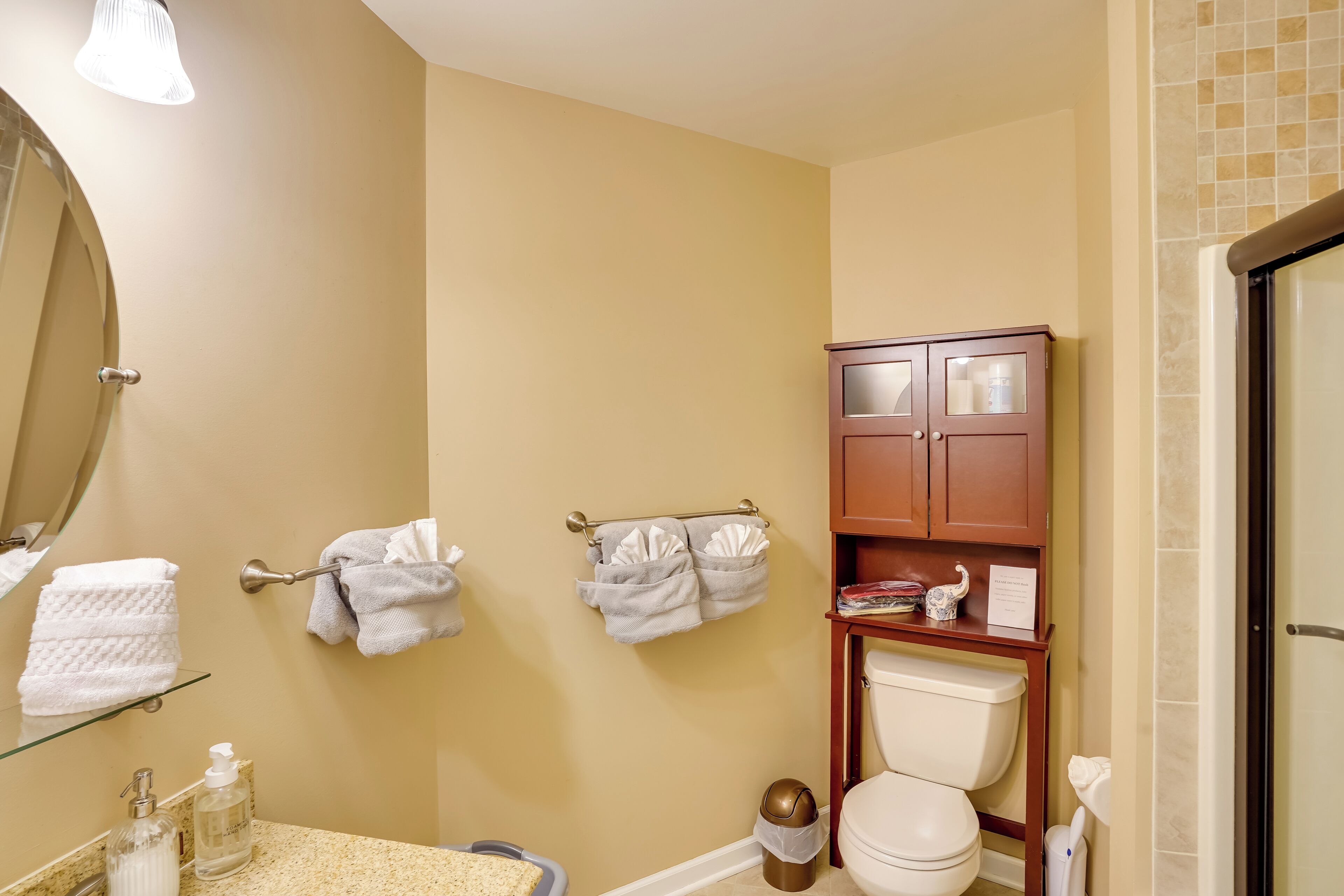 A bathroom with a toilet, a sink with a soap dispenser, a mirror, and a towel rack with towels.