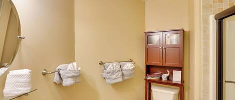 A bathroom with a toilet, a sink with a soap dispenser, a mirror, and a towel rack with towels.