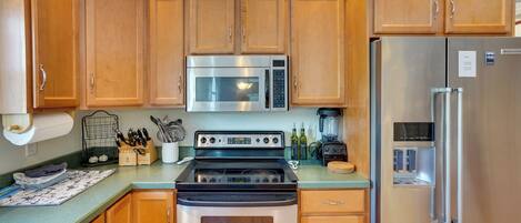 A kitchen with wooden cabinets, stainless steel appliances including a microwave, stove, and refrigerator, and a countertop with various kitchen items.