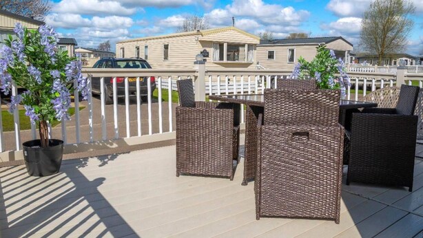 A patio area with wicker furniture, a covered seating area, and a view of a row of houses in the background. - Tattershall Lakes Private Hot Tub Lodge - Sleeps 6 (Lincoln)