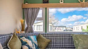 A living room with a sofa, a window with curtains, and a view of a residential area. - Tattershall Lakes Private Hot Tub Lodge - Sleeps 6 (Lincoln)