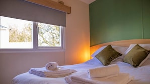 A neatly made bed with white linens and rolled towels, a green accent wall, and a window with a view of trees. - Tattershall Lakes Private Hot Tub Lodge - Sleeps 6 (Lincoln)