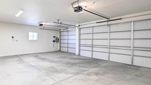A clean, empty garage with white garage doors, a ceiling-mounted projector, and a small window. - Modern Kingman Vacation Rental, 5 Mi to Dtwn! (Kingman)
