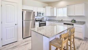 A modern kitchen with white cabinetry, stainless steel appliances, a granite countertop, and a built-in island with bar stools. - Modern Kingman Vacation Rental, 5 Mi to Dtwn! (Kingman)