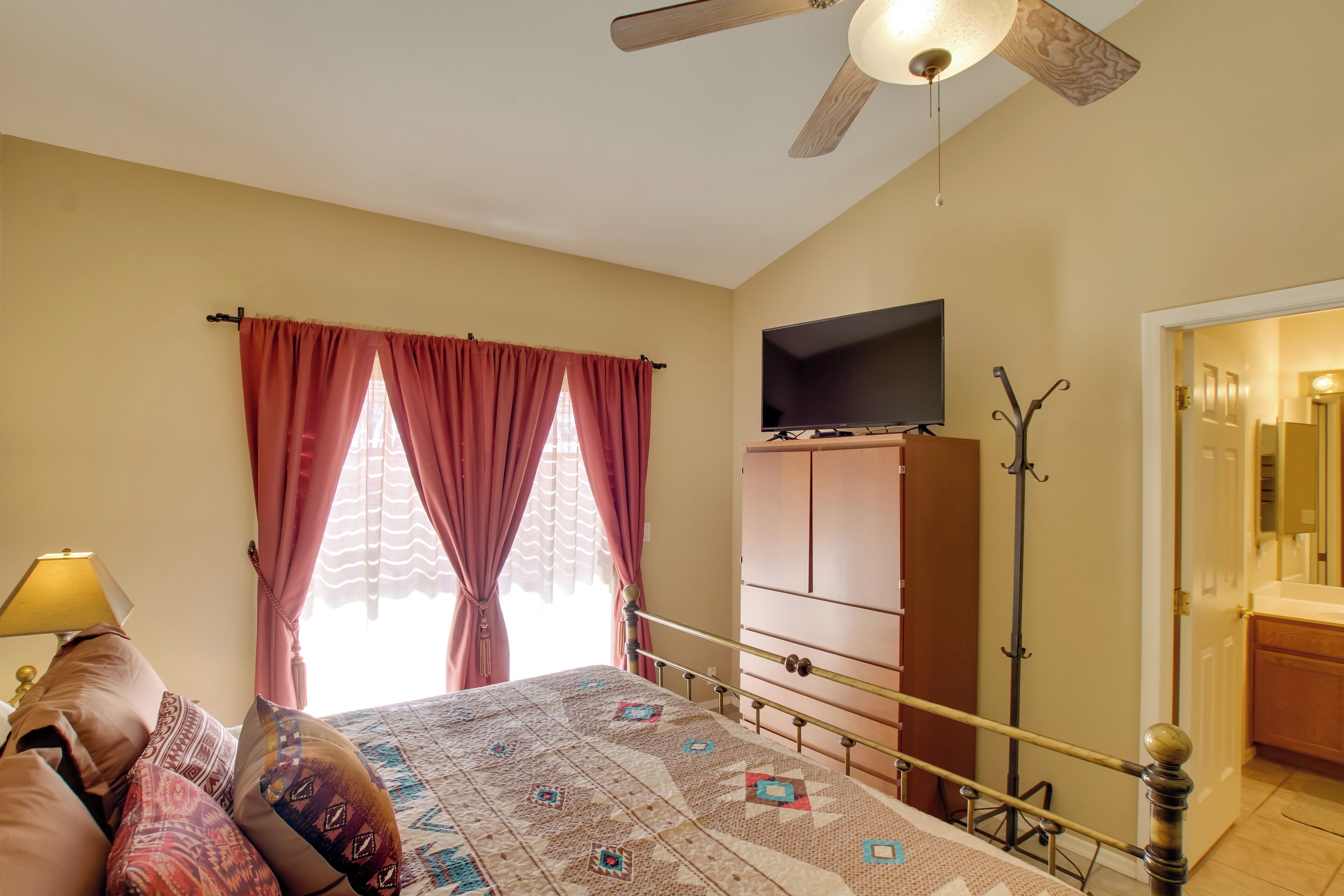 A bedroom with a bed, a TV mounted on the wall, a ceiling fan, and a wardrobe.