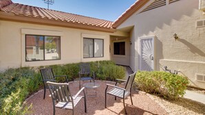 A patio with four chairs and a table, surrounded by gravel and plants, in front of a building with a tiled roof and white walls.
