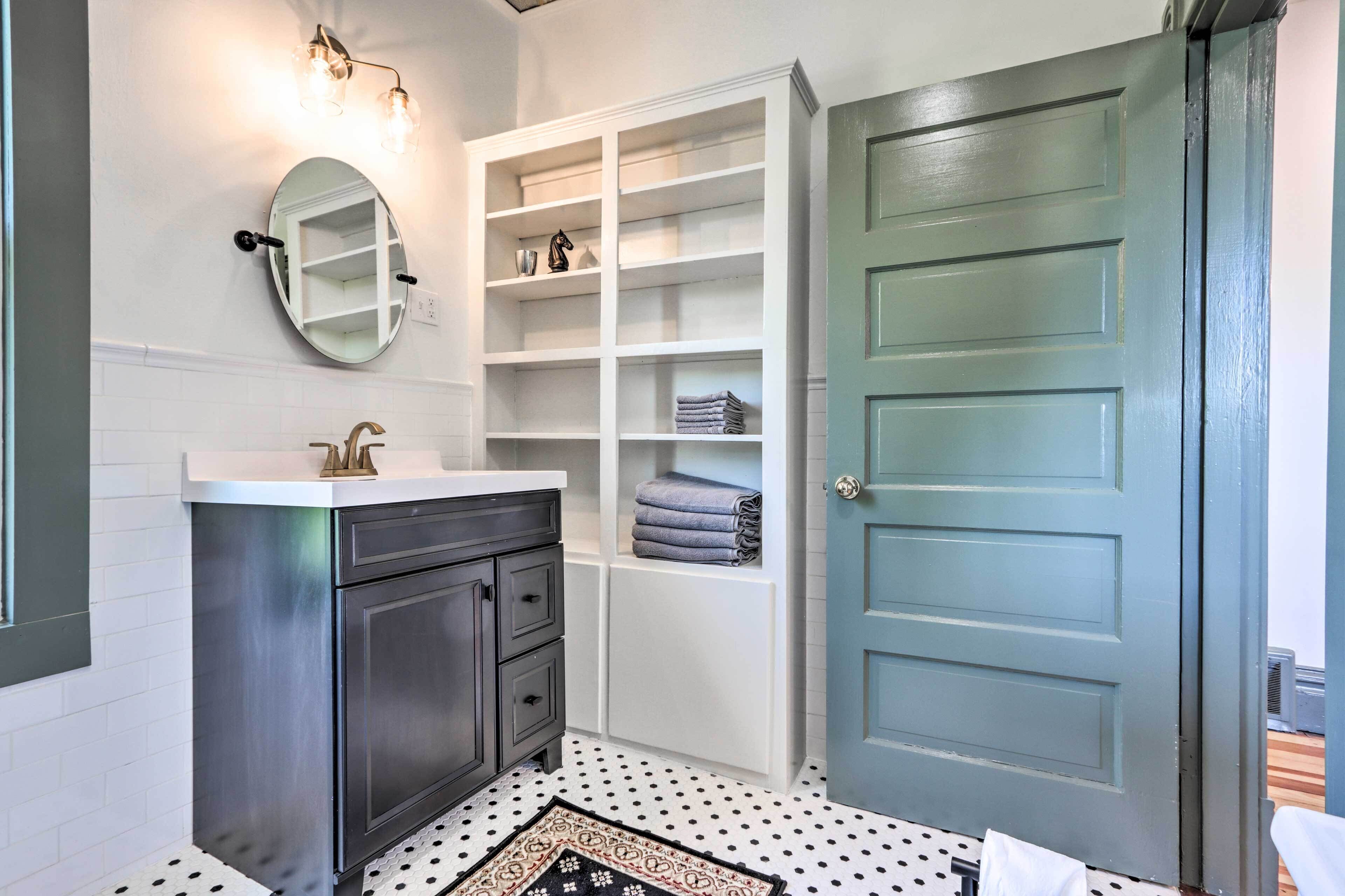 A bathroom with a white vanity, a mirror, a built-in shelf unit, and a patterned rug.