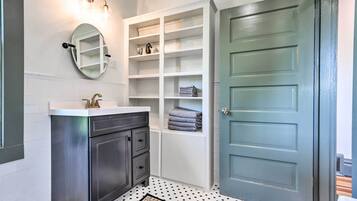 A bathroom with a white vanity, a mirror, a built-in shelf unit, and a patterned rug.