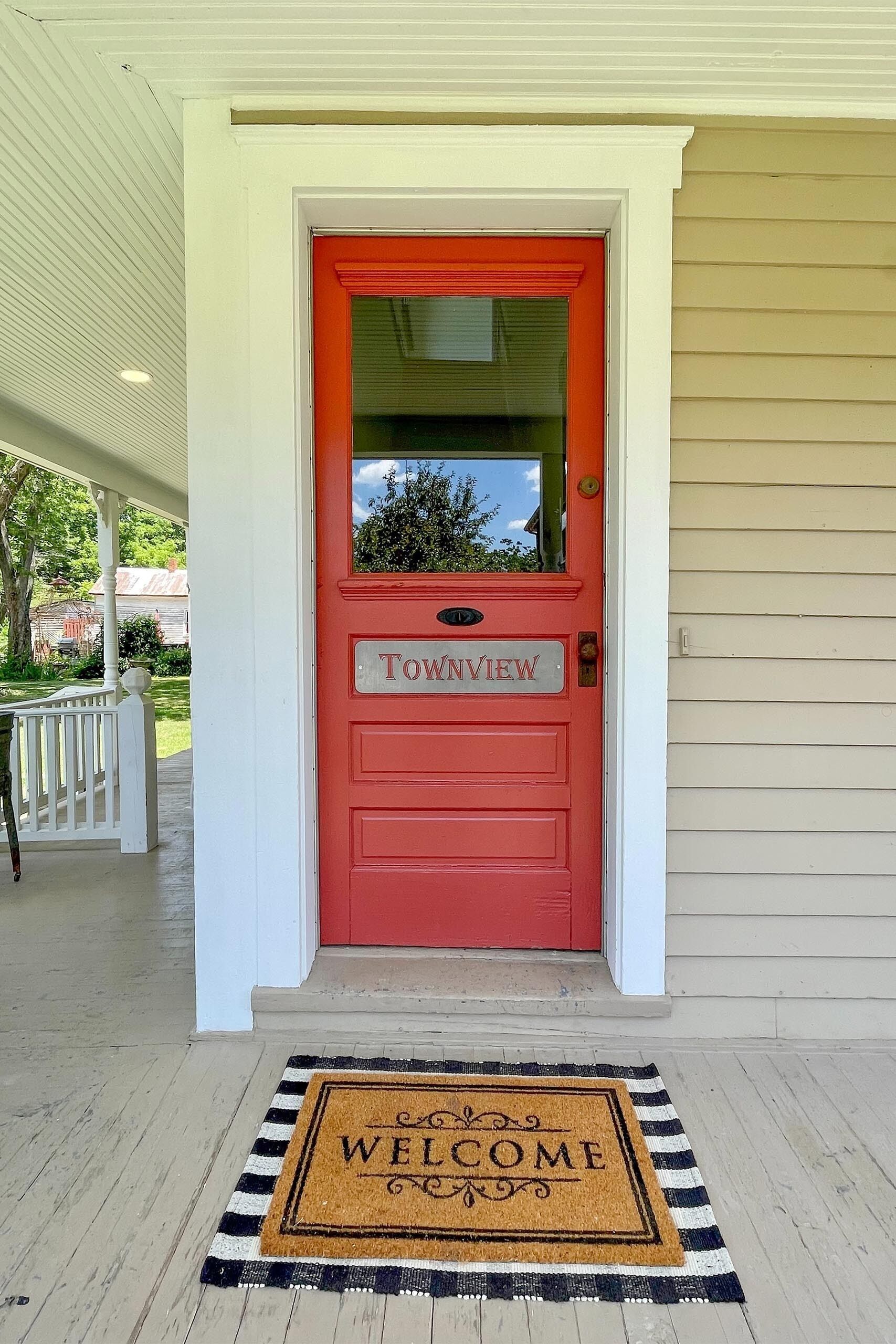 A red door with a sign reading "Townview" and a doormat with "WELCOME" on a porch.