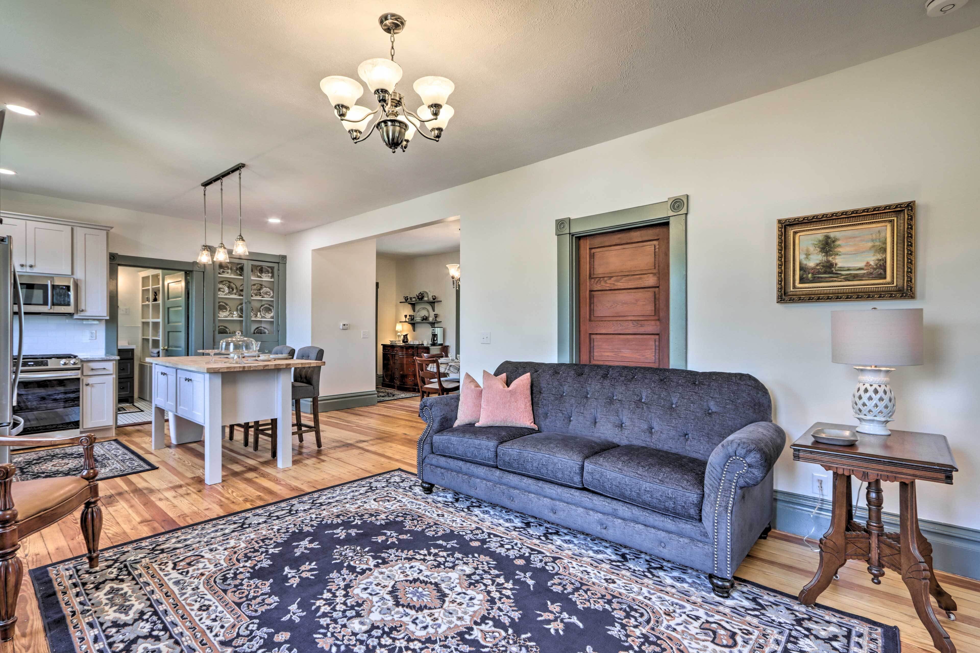 A living room with a grey sofa, a patterned rug, a chandelier, and a wooden door.