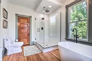 A modern bathroom with a glass-enclosed shower, a freestanding bathtub, and a wooden door.