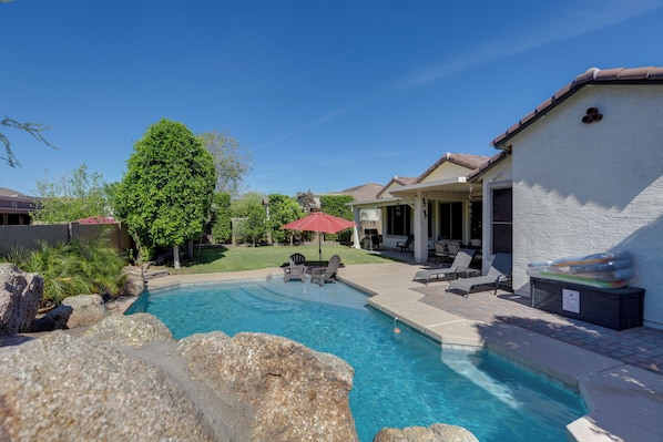 A backyard with a swimming pool, patio furniture, and a covered seating area.