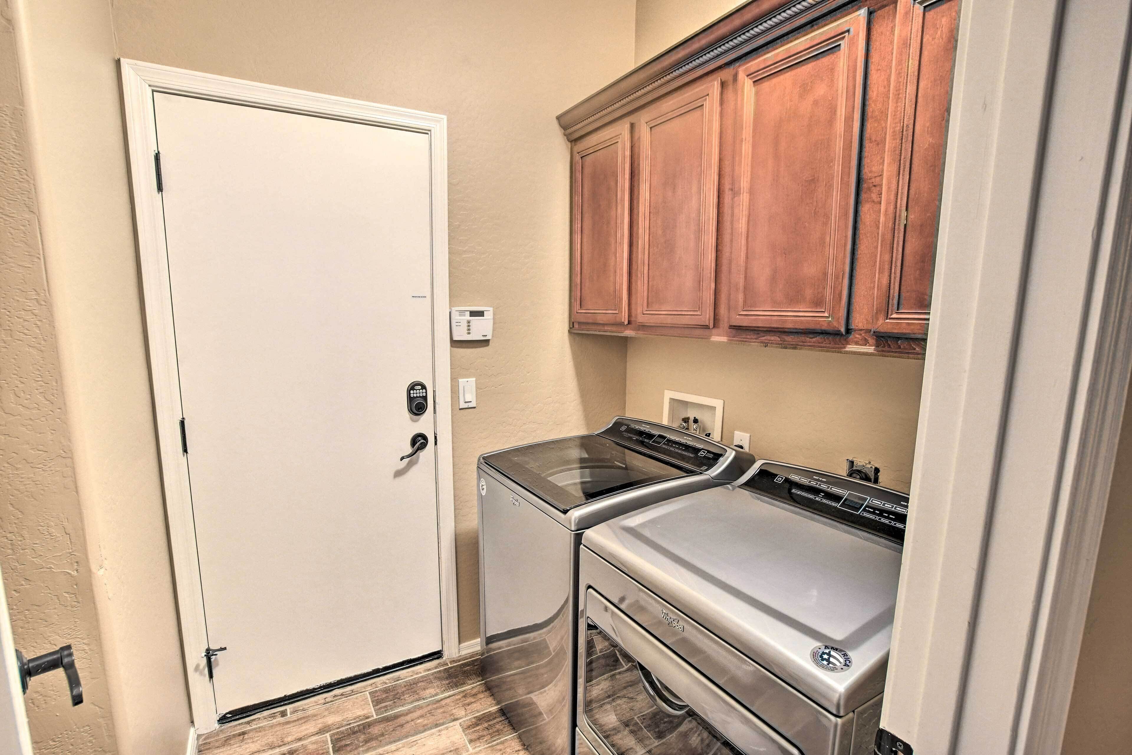 A laundry room with a white door, a washing machine, a dryer, and wooden cabinets.