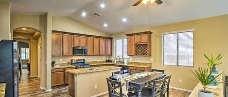 A modern kitchen with wooden cabinets, a granite countertop, and a dining area with a table and chairs.