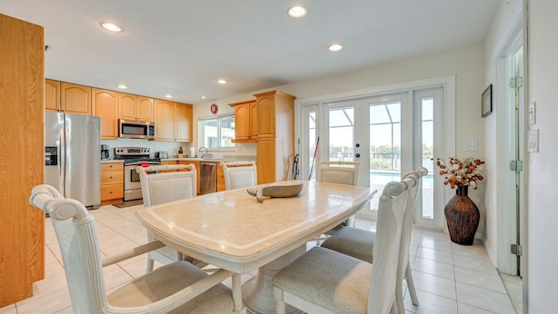 A modern kitchen with white cabinetry, a stainless steel refrigerator, a microwave, and a dining area with a white table and chairs. - Canalfront Port Charlotte Getaway w/ Boat Dock! (Port Charlotte)