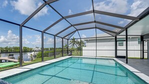A swimming pool with a glass enclosure, a view of a body of water, and a white building in the background. - Canalfront Port Charlotte Getaway w/ Boat Dock! (Port Charlotte)