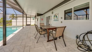 A covered outdoor area with a pool, a table with chairs, and a hose on the floor. - Canalfront Port Charlotte Getaway w/ Boat Dock! (Port Charlotte)