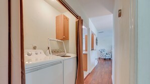 A laundry area with a washer and dryer, wooden cabinets, and a patterned chair in the background. - Canalfront Port Charlotte Getaway w/ Boat Dock! (Port Charlotte)