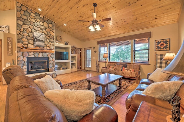 A cozy living room with a stone fireplace, leather sofas, a wooden ceiling, and a television.