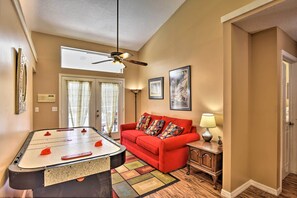 A cozy living room with a foosball table, a red sofa, and a ceiling fan. - Cocoa Beach Paradise: Screened Pool, Patio + Games (Merritt Island)