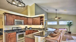 A kitchen with a central island, stainless steel appliances, and brown cabinetry. - Cocoa Beach Paradise: Screened Pool, Patio + Games (Merritt Island)