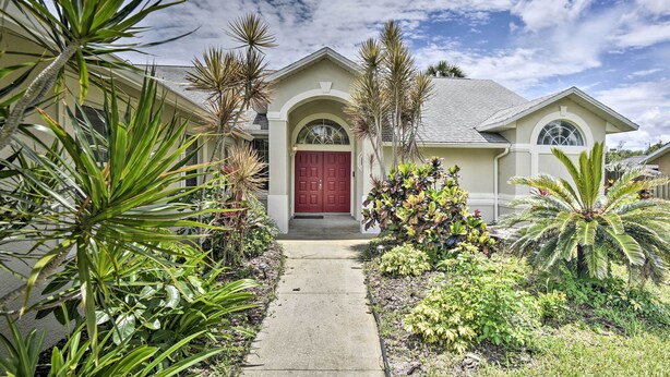 A house with a red door, a covered front porch, and a garden with various plants. - Cocoa Beach Paradise: Screened Pool, Patio + Games (Merritt Island)