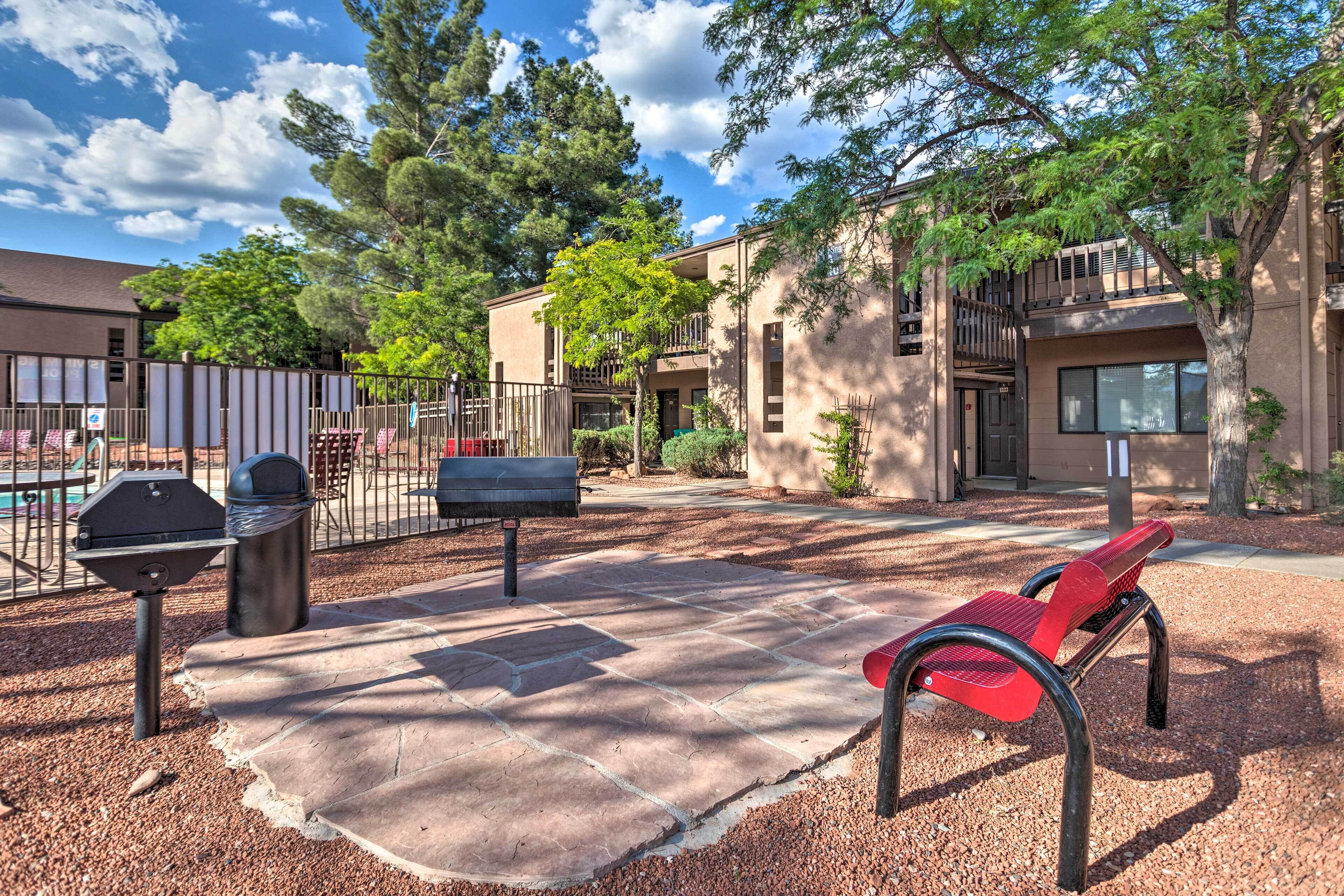 Un espace extérieur aménagé en patio, avec un barbecue, un banc rouge et un chemin pavé, le tout entouré d’arbres et d’immeubles.