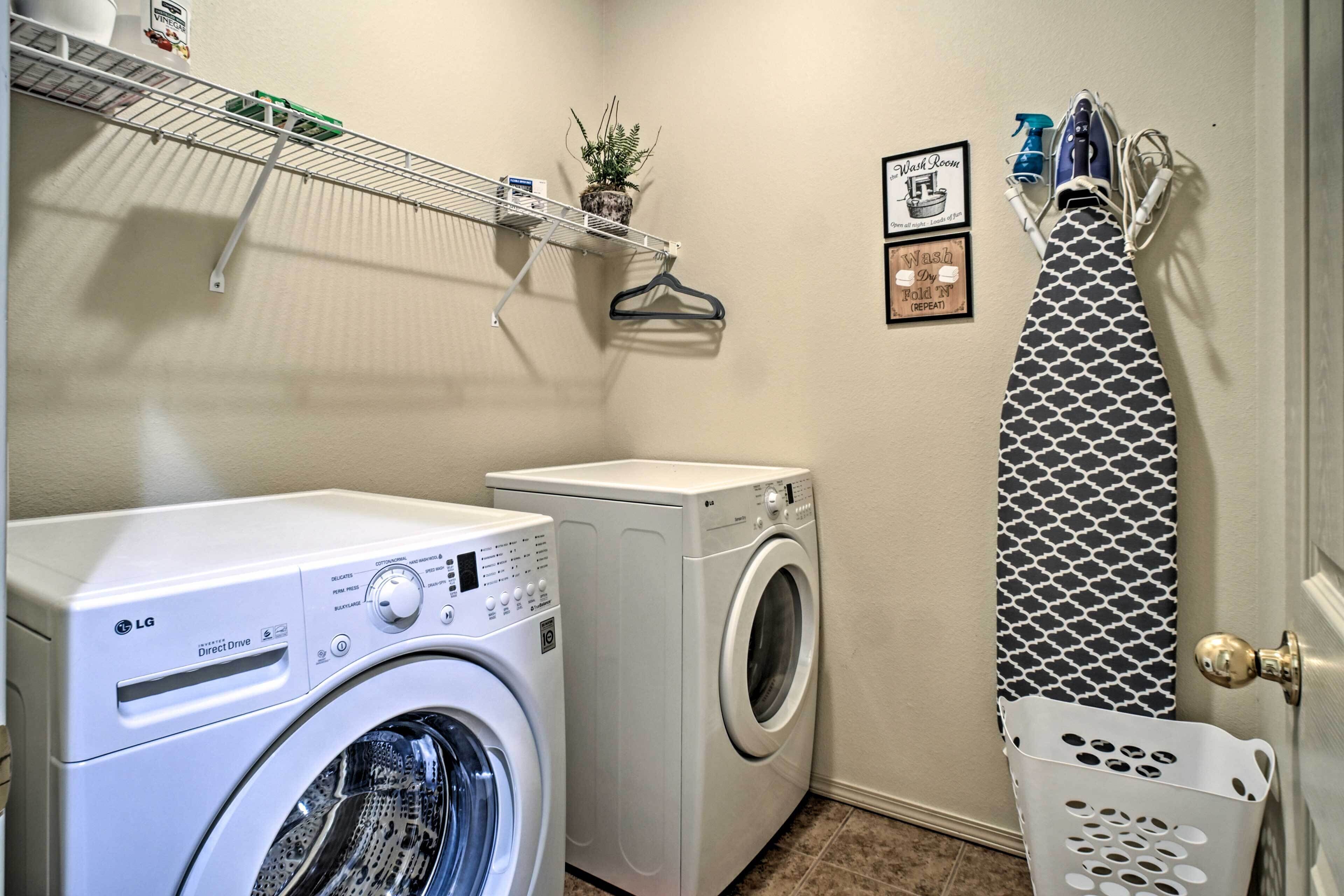 A laundry area with two washing machines, a drying rack, and a wall-mounted shelf with a plant and cleaning supplies.