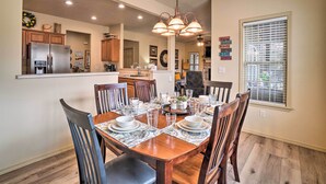 A dining room with a wooden table set for six, surrounded by chairs. A chandelier hangs above, and a window with blinds is visible to the right. - Branson West Villa w/ Golf Course View & Pool! (Branson West)