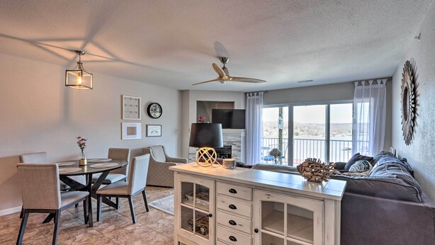 A modern living room with a dining area, a ceiling fan, a large window, and a view of the outdoors. - Relax Poolside! 'serenity at the Lake' in Ozarks (Camdenton)